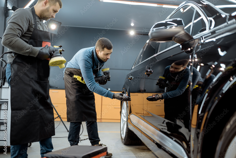 Car service workers examining glossy vehicle body coating for scratches after the polishing procedur