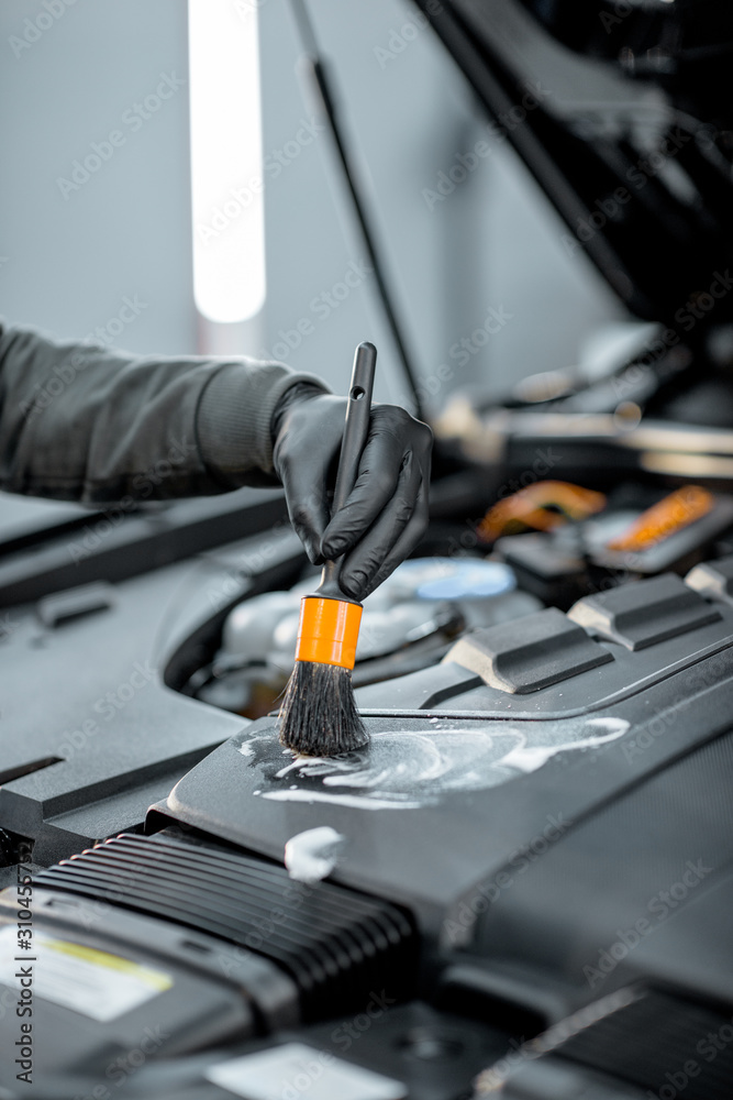 Man performs a professional car cleaning, washing engine with brush and detergent at the service sta