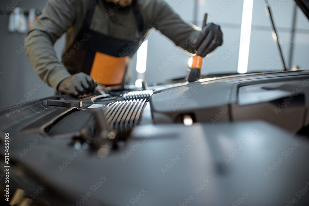 Man performs a professional car cleaning, washing engine with brush and detergent at the service sta