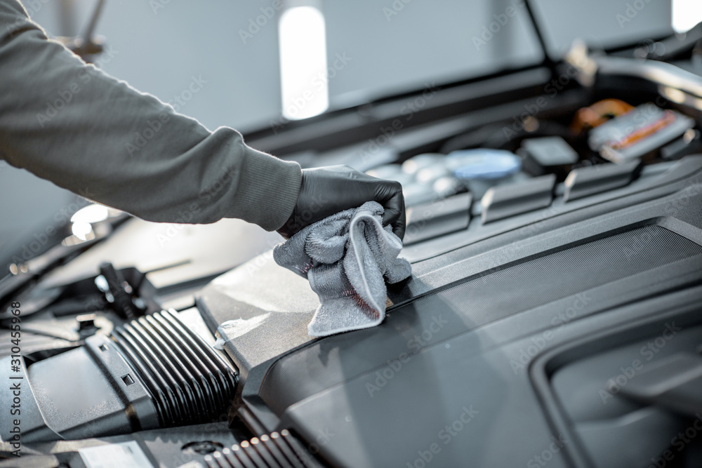 Man performs a professional car cleaning, wiping engine with microfibre at the service station, clos