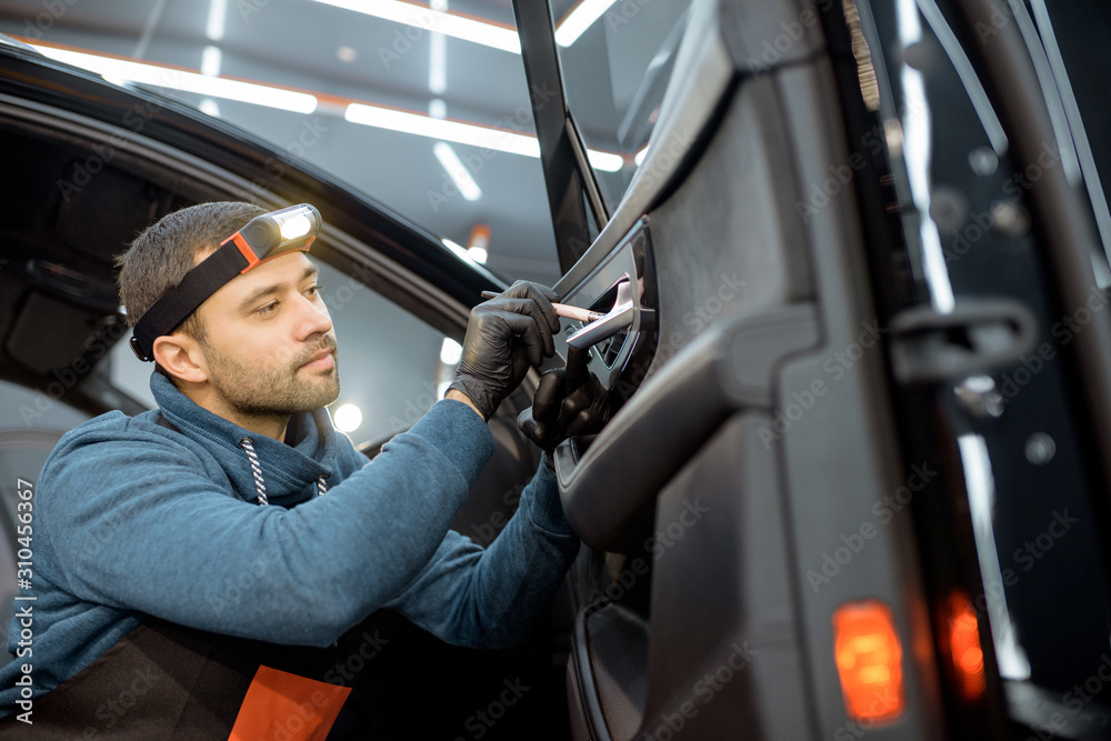 Car service worker in uniform provides a professional vehicle interior cleaning, wiping door panel w