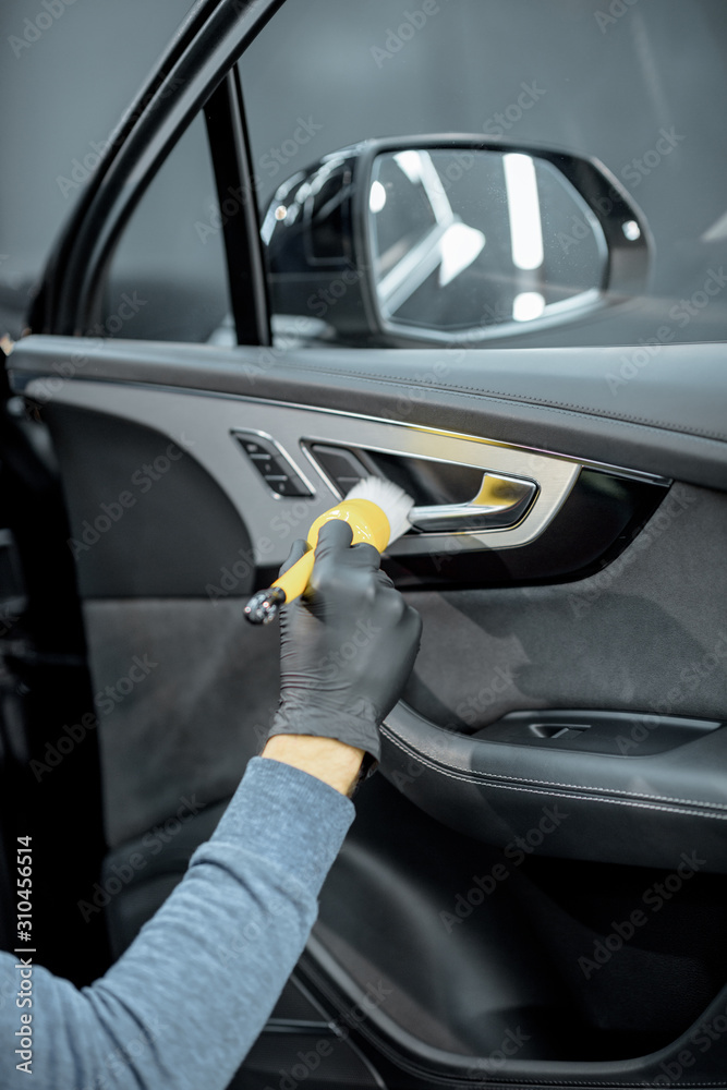 Worker provides a professional vehicle interior cleaning, wiping door panel with a brush at the car 