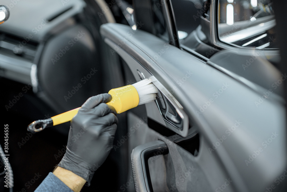 Worker provides a professional vehicle interior cleaning, wiping door panel with a brush at the car 