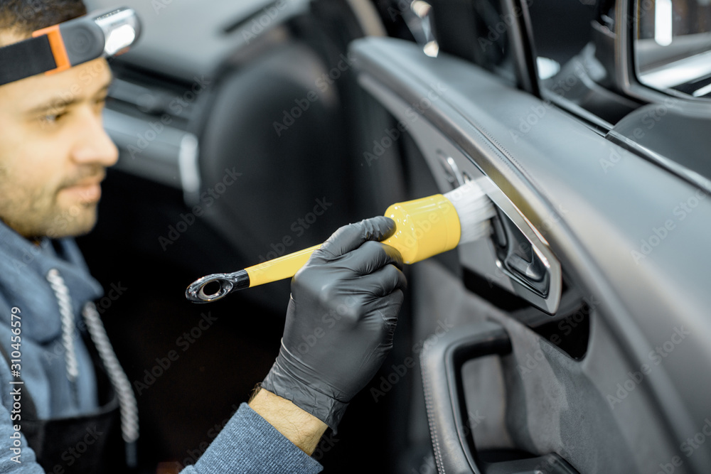 Car service worker in uniform provides a professional vehicle interior cleaning, wiping door panel w