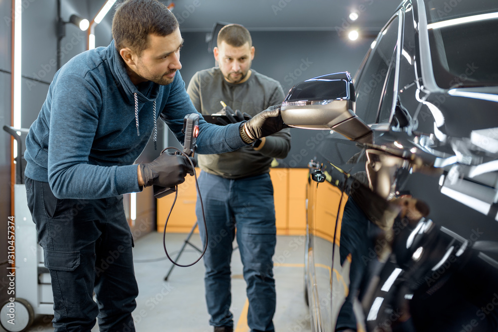 Two car service workers examining vehicle body for scratches and damages while taking a car for prof