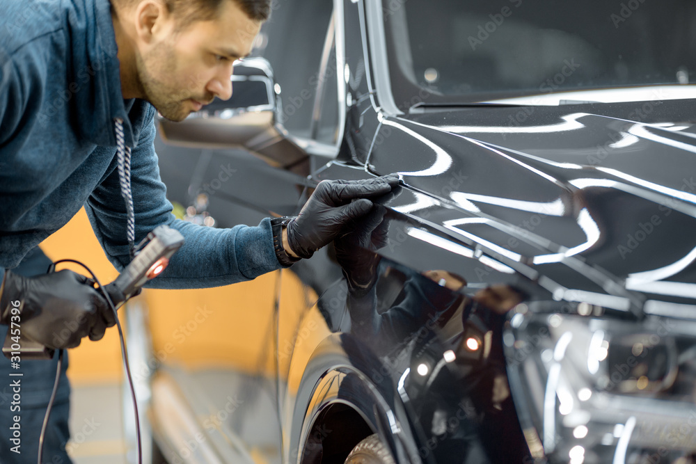 Car service worker examining vehicle body for scratches and damages, taking a car for professional a