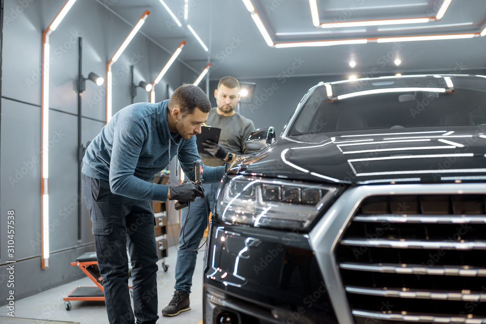 Two car service workers examining vehicle body for scratches and damages while taking a car for prof