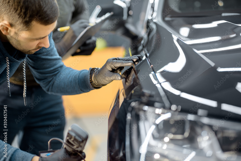 Car service worker examining vehicle body for scratches and damages, taking a car for professional a