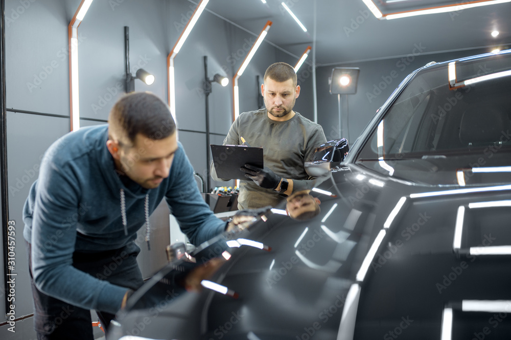 Two car service workers examining vehicle body for scratches and damages while taking a car for prof