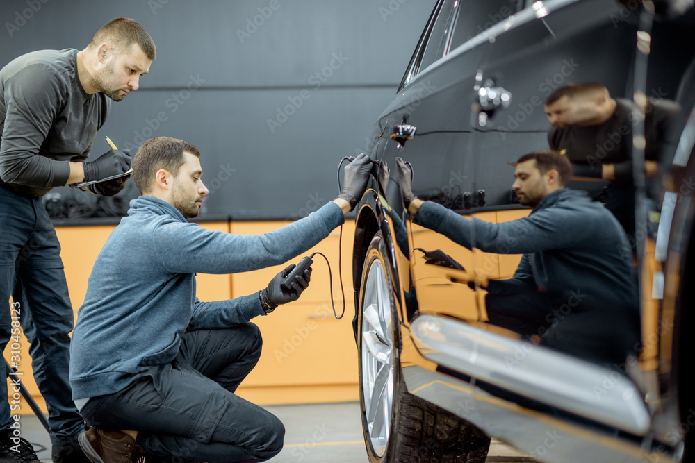 Two car service workers examining vehicle body for scratches and damages while taking a car for prof