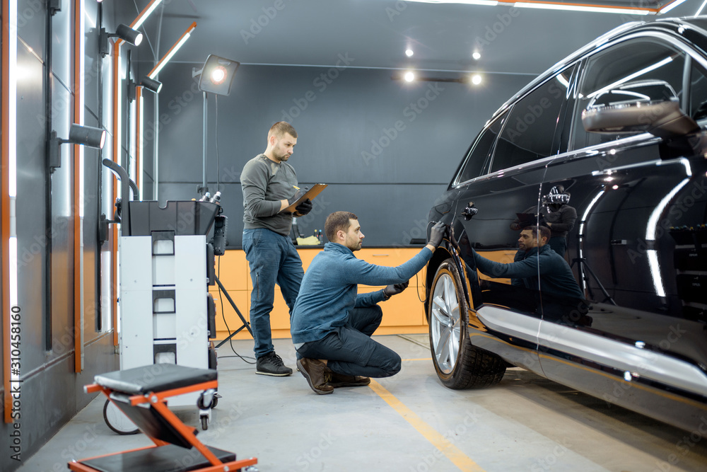 Two car service workers examining vehicle body for scratches and damages while taking a car for prof