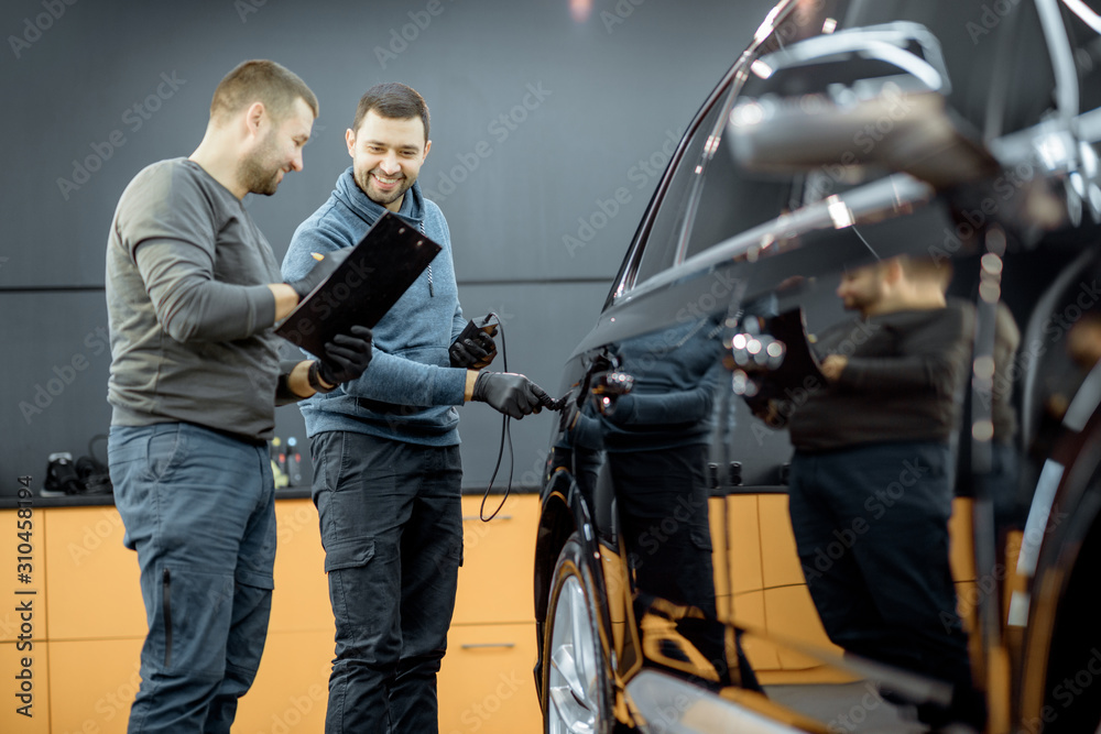 Two car service workers examining vehicle body for scratches and damages while taking a car for prof