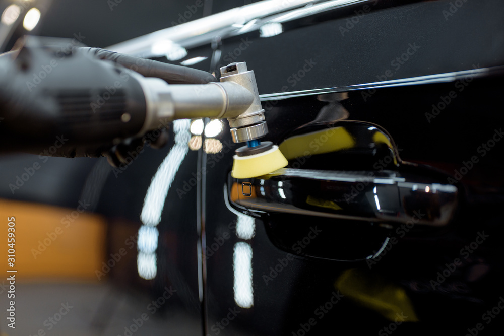 Car service worker polishing vehicle door handle with special wax from scratches, close-up. Professi