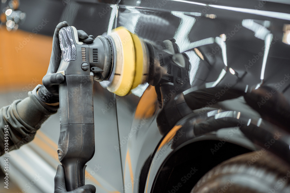 Car service worker polishing vehicle body with special wax from scratches, close-up. Professional ca