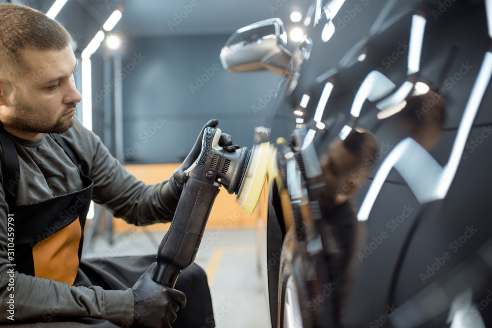 Worker polishing vehicle body with special grinder and wax from scratches at the car service station