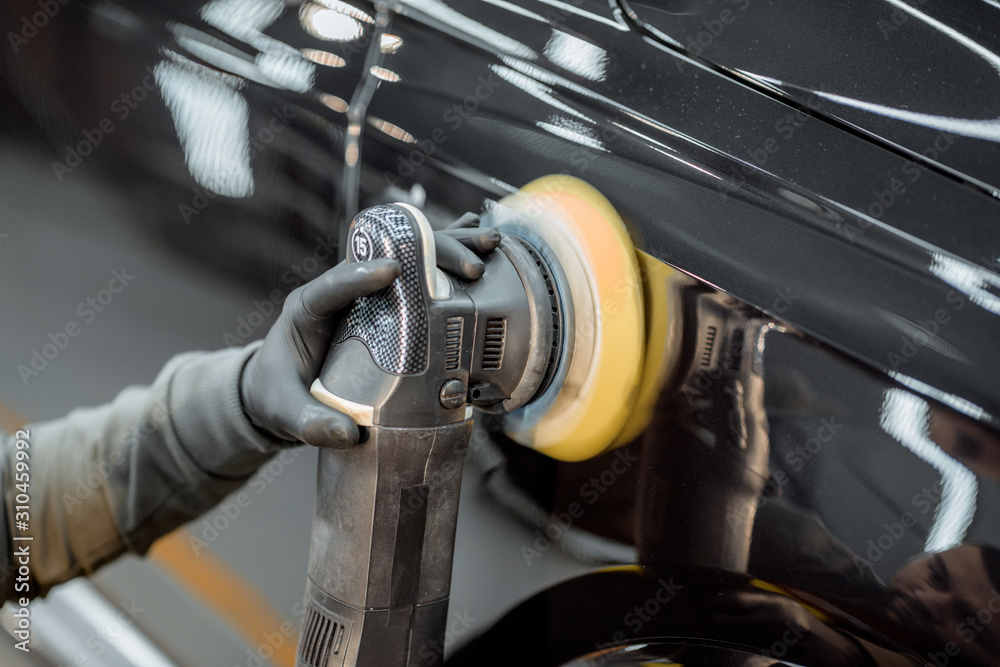 Car service worker polishing vehicle body with special wax from scratches, close-up. Professional ca