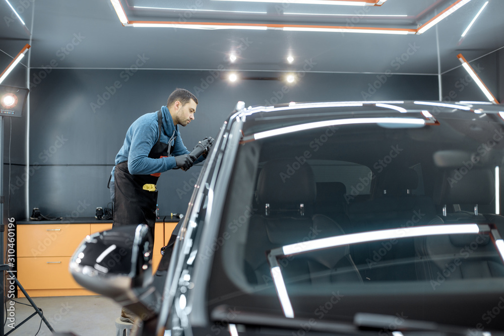 Worker polishing vehicle body with special grinder and wax from scratches at the car service station