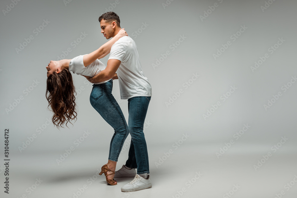 side view of dancers in t-shirts and jeans dancing bachata on grey background