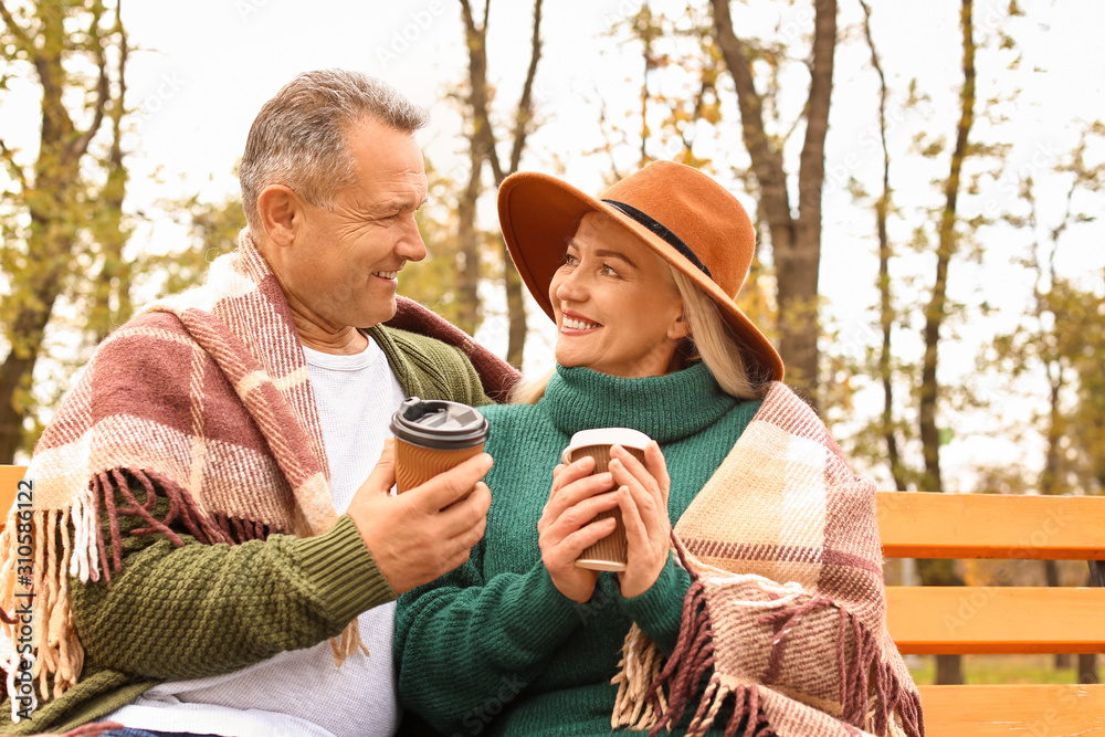 Happy mature couple drinking coffee in autumn park