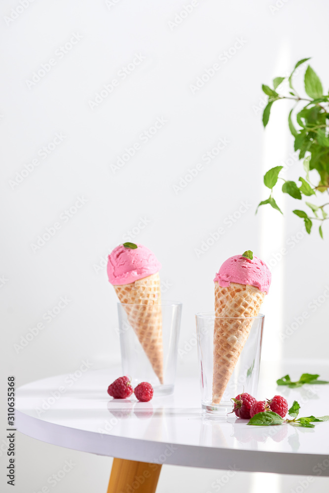 Waffle cone filled with fresh raspberry ice cream in glass cup with fresh raspberry sitting on table