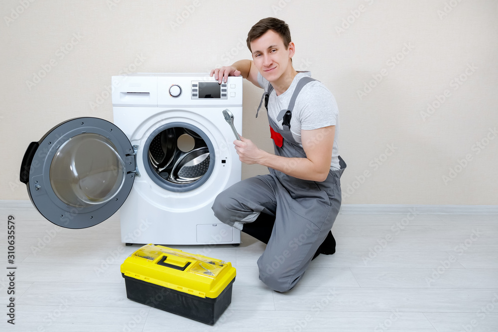 professional master with wrench and toolbox near modern washing machine on wooden floor near beige w