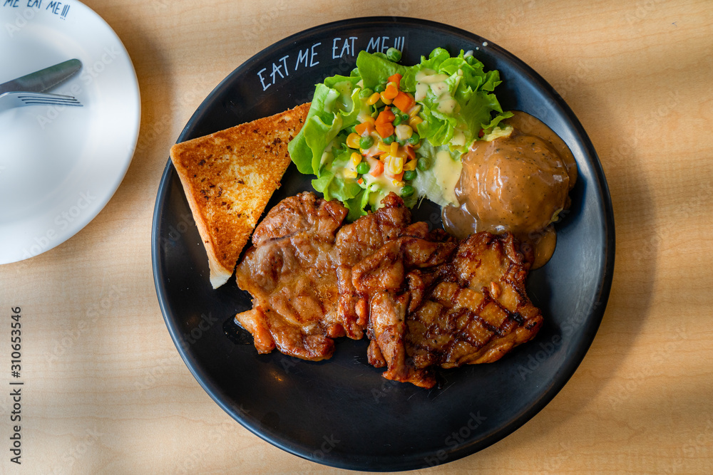 steak,salad,mashed potato and  garlic bread in black plate set on wood table with window shadow