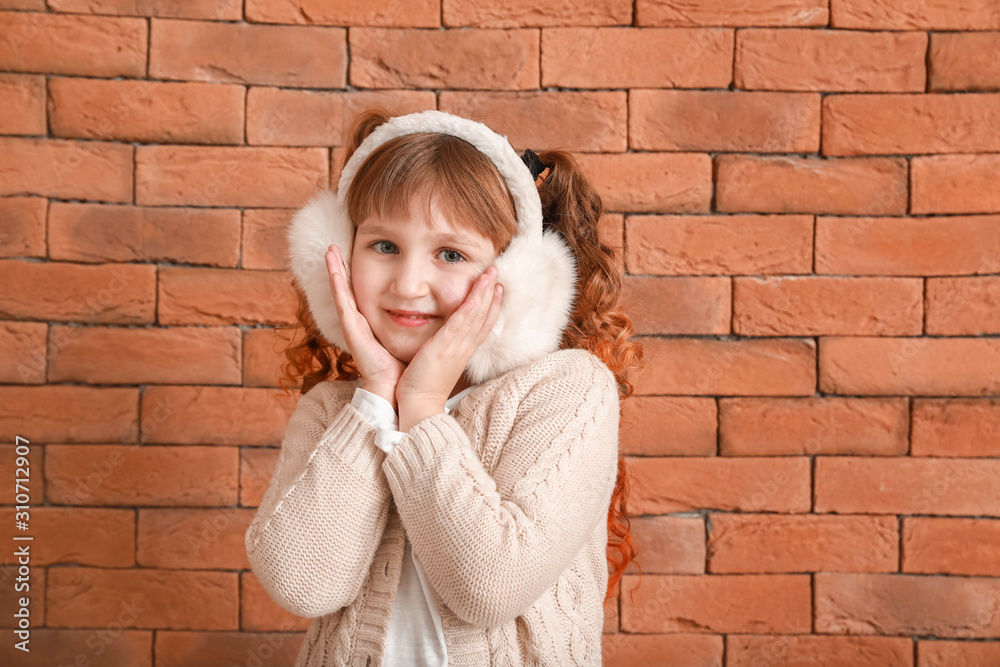 Cute little girl in winter clothes near brick wall