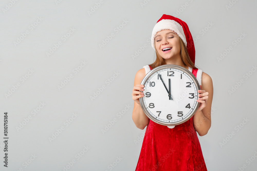 Young woman in Santa costume and with clock on light background. Christmas countdown concept