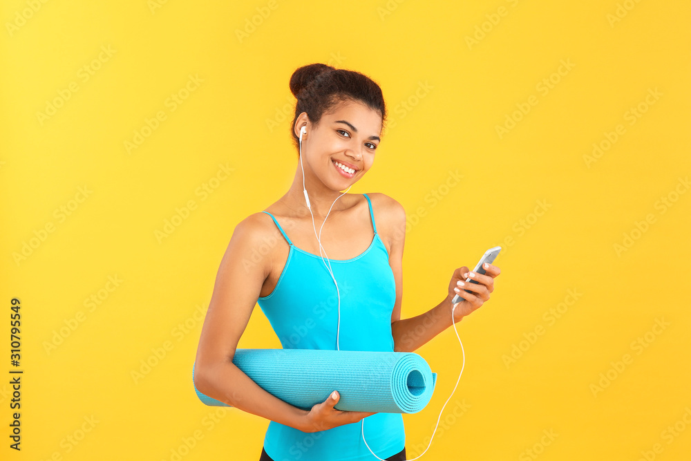 Sporty African-American woman with yoga mat and mobile phone on color background