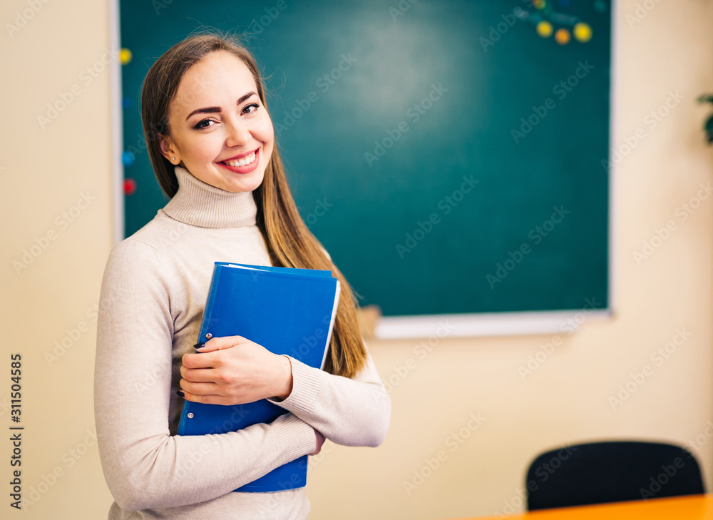 学生女孩站在教室干净的黑板旁，手里拿着文件夹。学校理念。