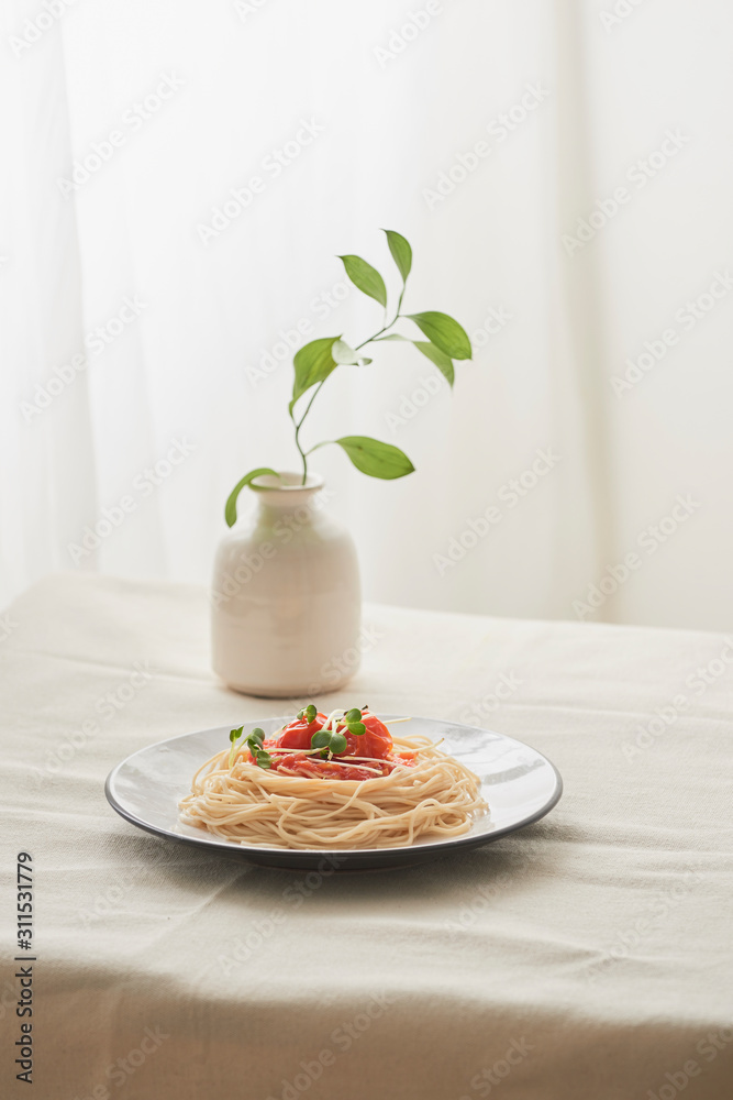 食物，白盘子里的意大利肉酱意大利面和白色桌子上的一瓶植物