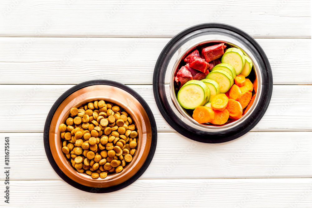 Healthy feed for cats and dogs. Bowls full of dry feed, meat and vegetables on white wooden backgrou