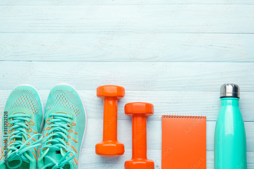 Dumbbells with notebook, shoes and bottle of water on white wooden background