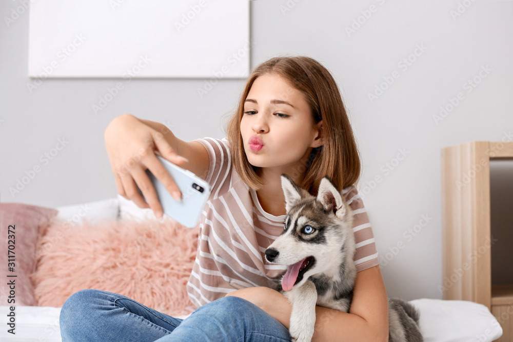 Cute teenage girl with funny husky puppy taking selfie on bed at home