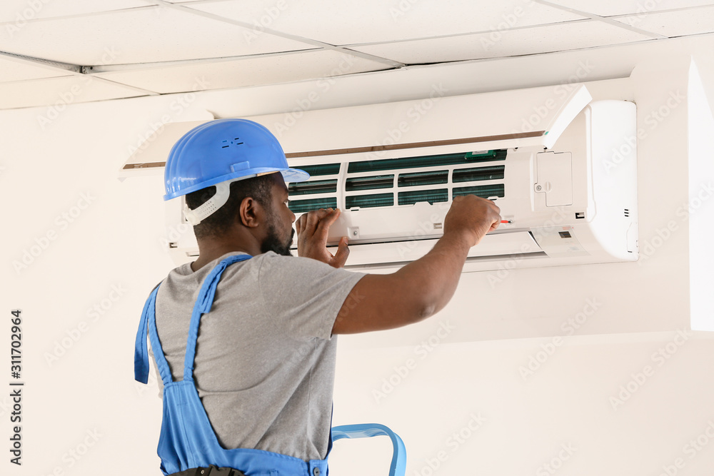 African-American electrician repairing air conditioner indoors