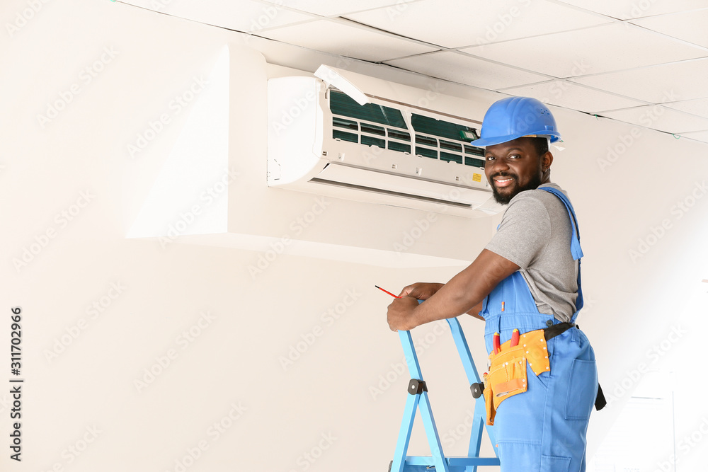 African-American electrician repairing air conditioner indoors