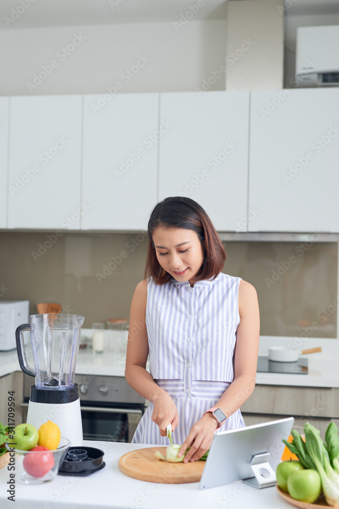 亚洲女人在厨房里切菜，面前放着平板电脑