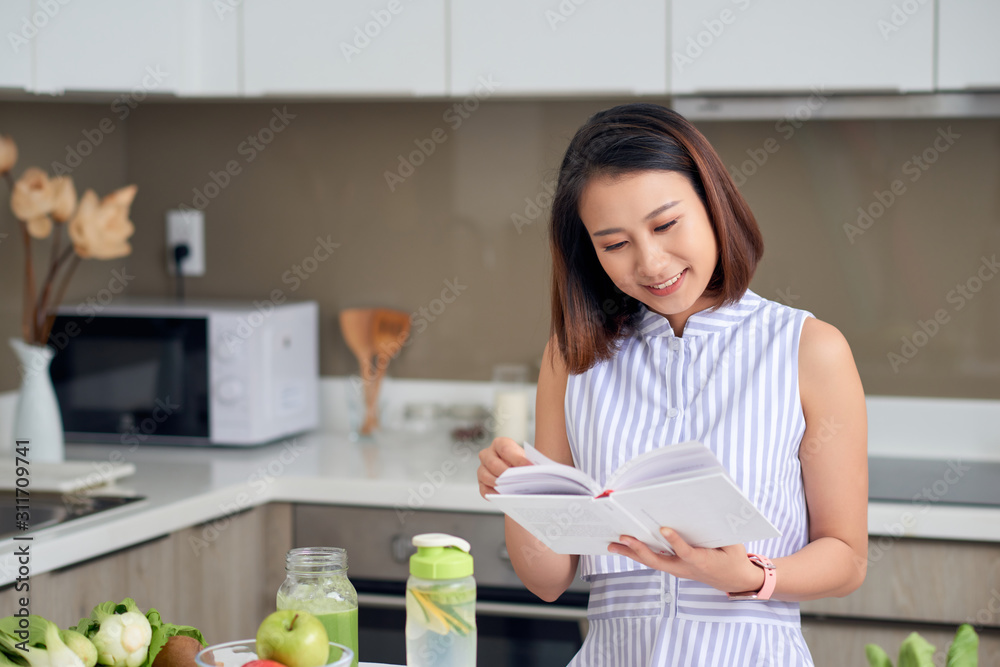 漂亮的女人在厨房里阅读排毒饮料配方。