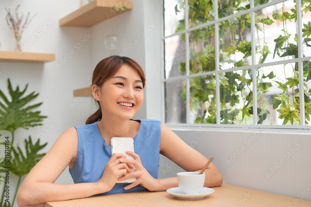 快乐的年轻亚洲女人一边打电话一边喝咖啡