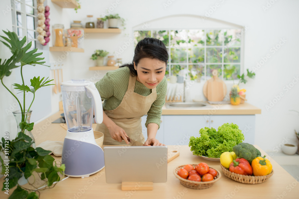 Woman In Kitchen Following Recipe On Digital Tablet