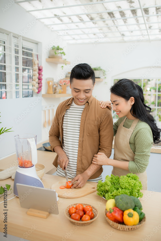 Portrait of a pretty young couple cooking together according to a recipe on a tablet computer