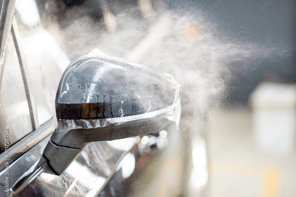 Spraying water on a car mirror during a protective film applying process at the vehicle service stat