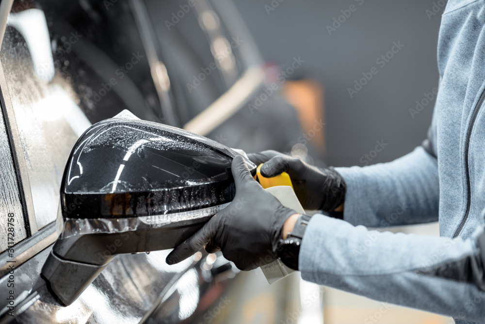 Man applying sticking protective film on a car mirror at the vehicle service station, cllose-up. Con