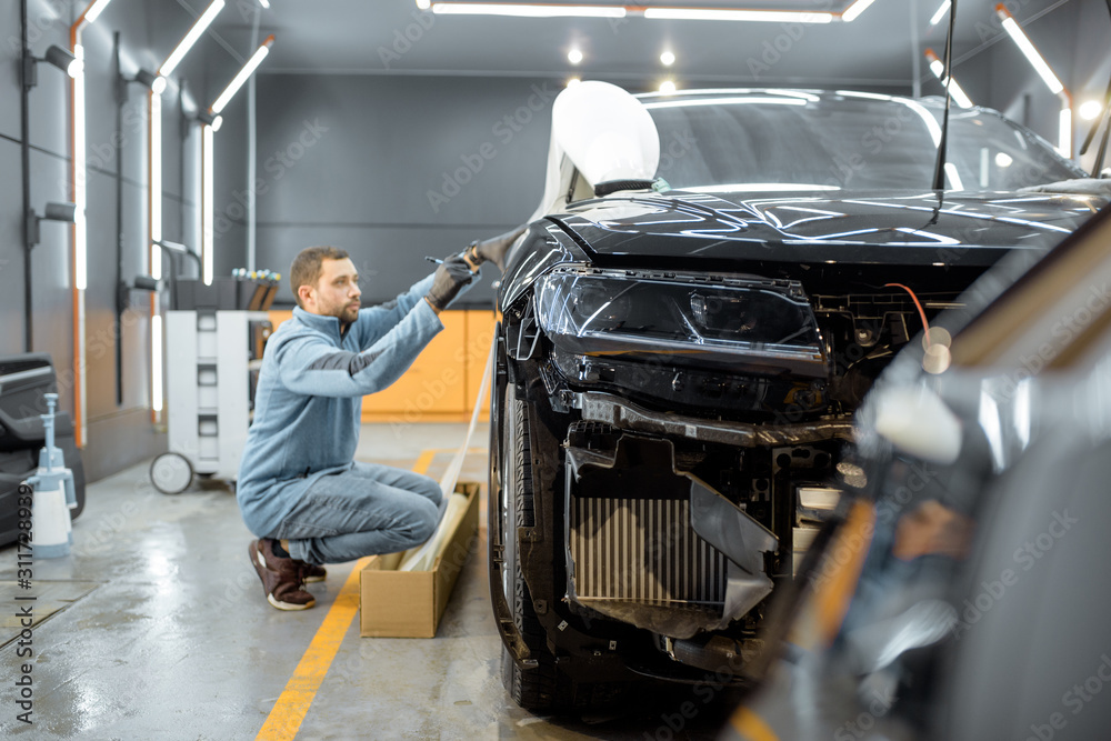 Man preparing protective film for sticking on a car body, marking it to with a pen at the vehicle se