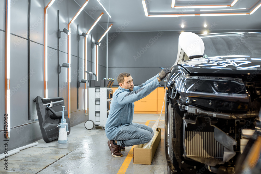 Man preparing protective film for sticking on a car body, marking it to with a pen at the vehicle se