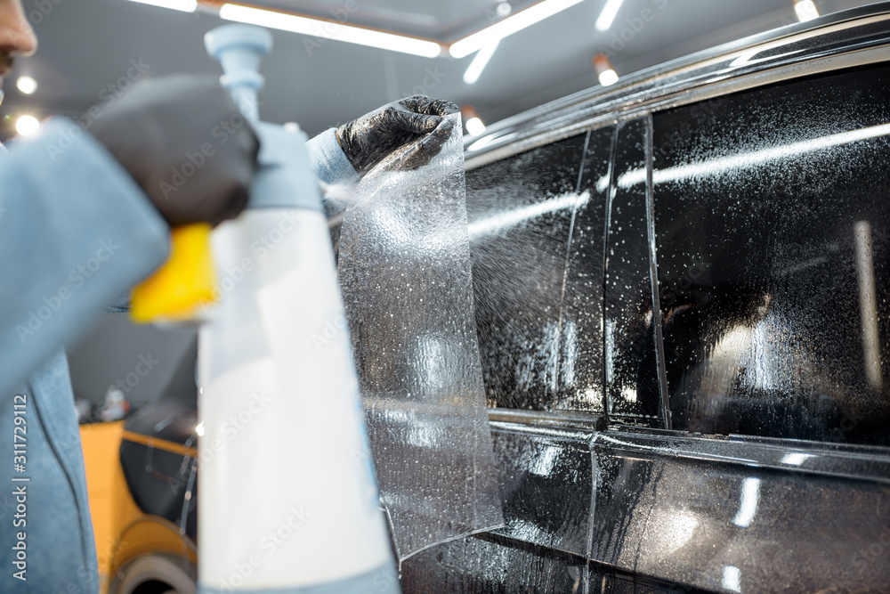 Car service worker sticking anti-gravel film on a window frame for protection at the detailing vehic