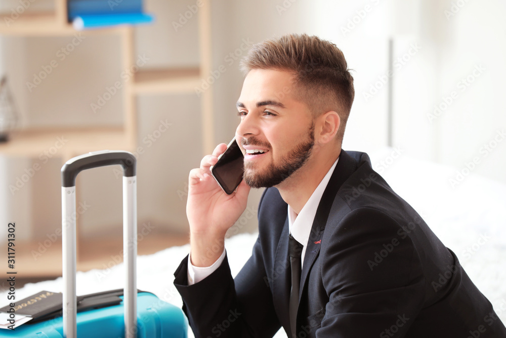 Young man with luggage for business trip talking by phone at home