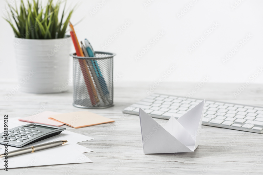 Wooden office desk with white origami boat.