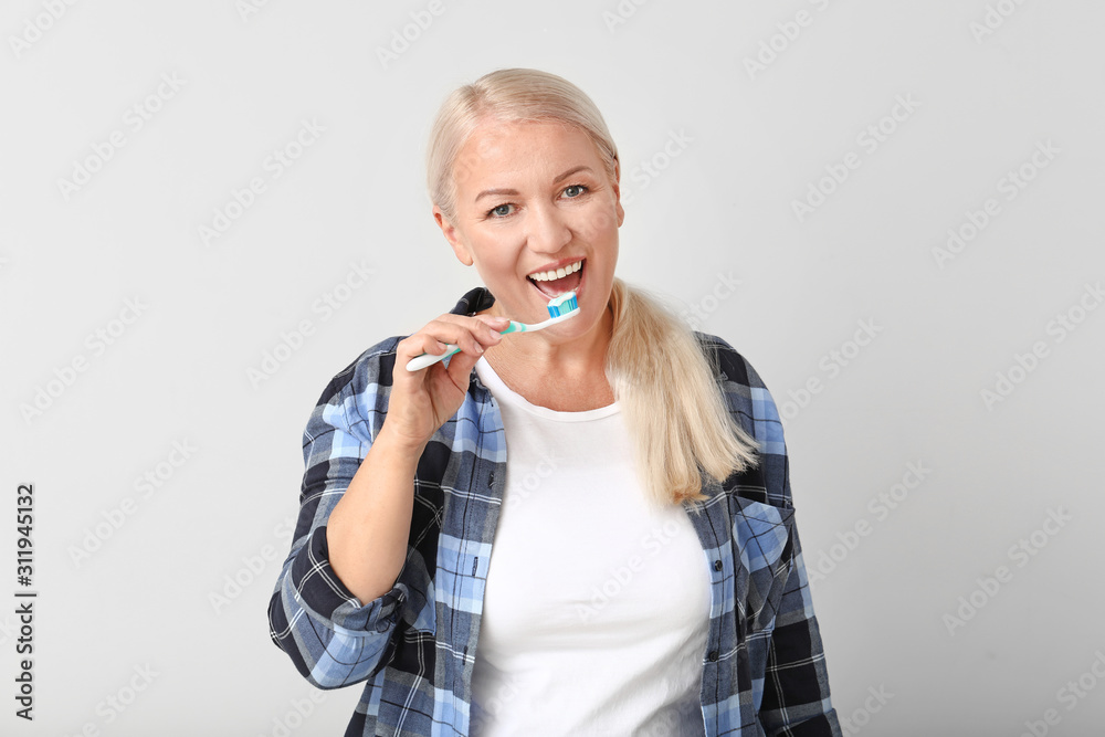 Mature woman brushing teeth on light background