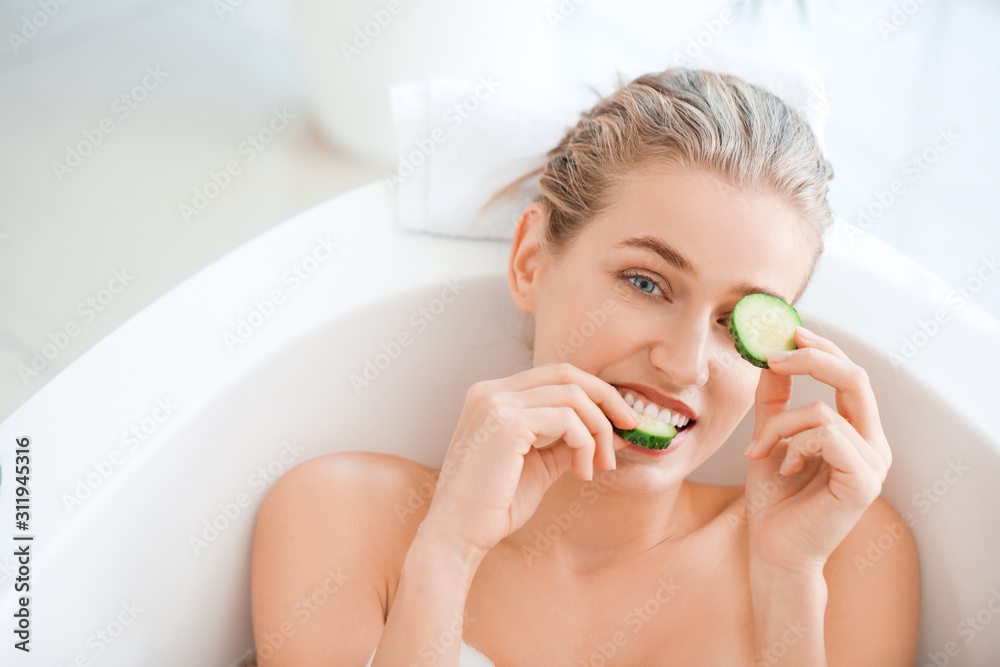 Beautiful young woman with cucumber slices lying in bathroom